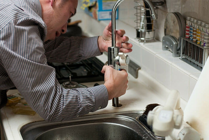 Plumber repairing pipework beneath a kitchen sink